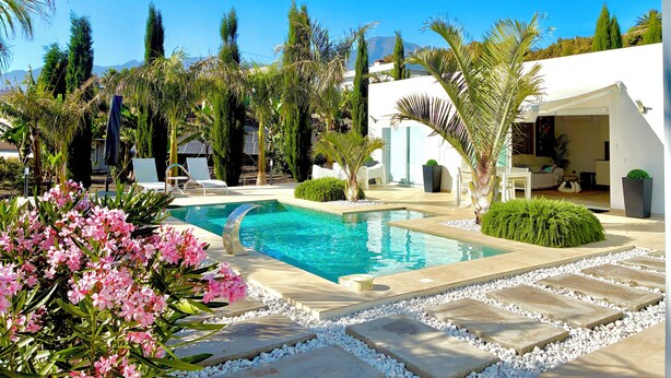 Une piscine entourée de chaises blanches, un bâtiment blanc et des palmiers.