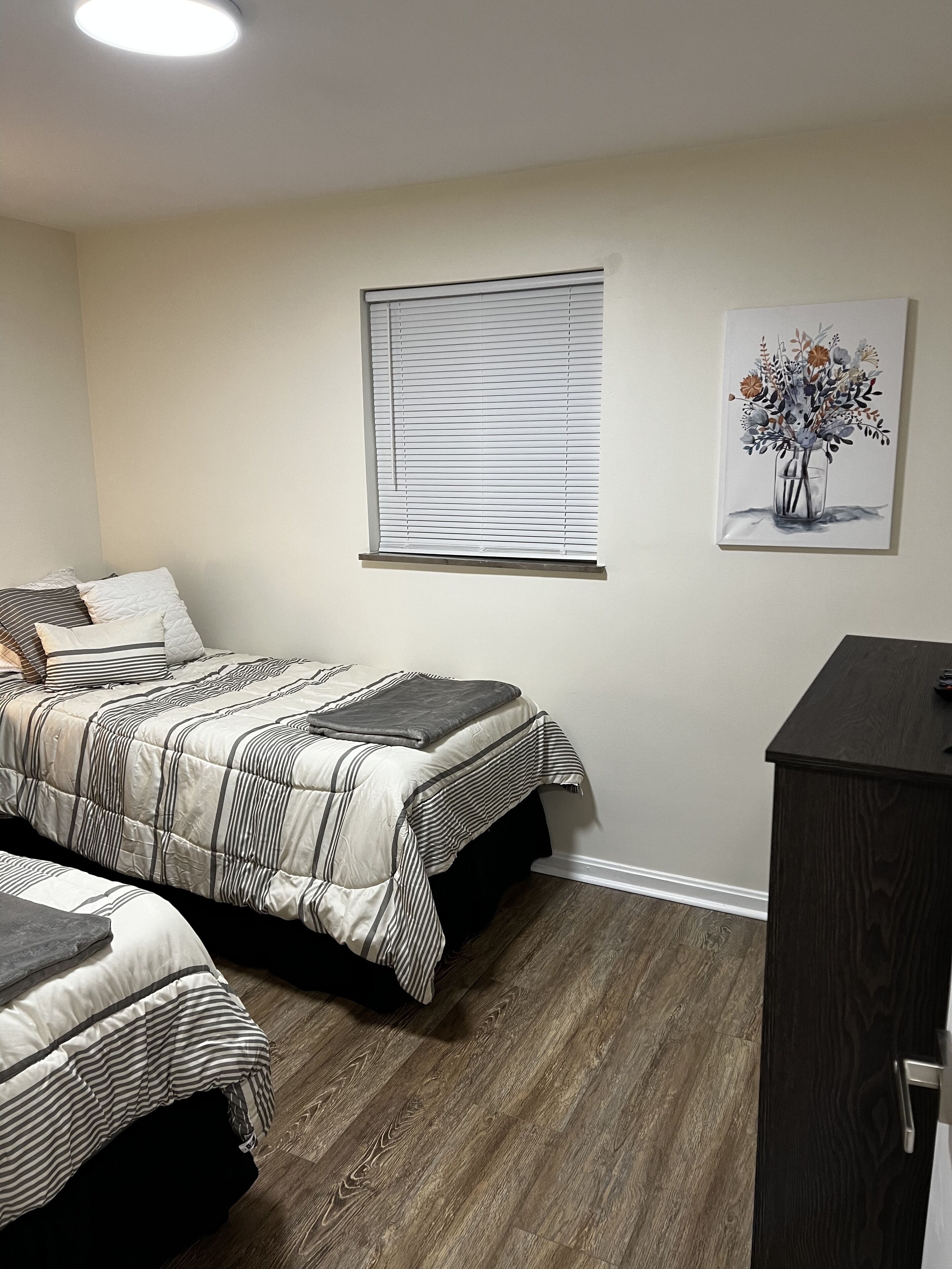 Une chambre à coucher avec un lit, une table de chevet, une fenêtre avec des stores et un tableau au mur.