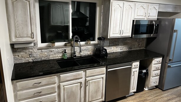 A kitchen with white cabinets, a black countertop, a built-in microwave, and a stainless steel refrigerator.