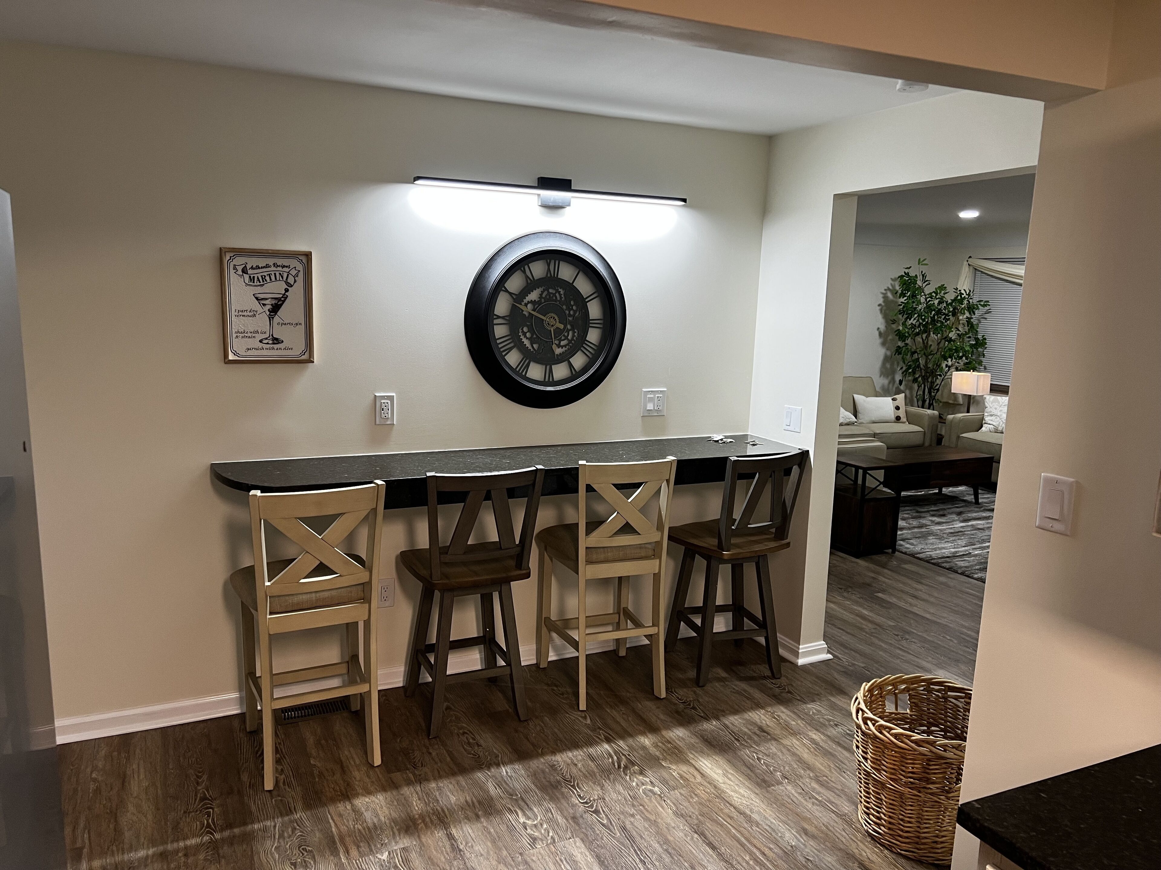 Une cuisine avec un coin bar, des chaises en bois, une horloge et un tableau encadré au mur.