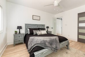 Une chambre Ă coucher avec un lit, des tables de chevet, un ventilateur de plafond et une porte.