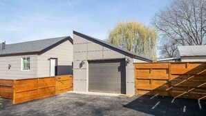 Un bâtiment d’un seul étage avec un garage, une cour clôturée et un arbre en arrière-plan.