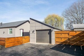 A single-story building with a garage, a fenced yard, and a tree in the background.