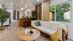 A modern living room with a sofa, a coffee table, and a kitchen area in the background. - Bali Inspired | Ping-Pong | Yoga | Massage | Bocce (Austin)