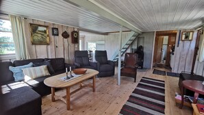Un salon chaleureux avec un plancher en bois, un canapé, deux fauteuils, une table basse et une cheminée.