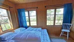Une pièce en bois avec un lit, deux fenêtres et une chaise.