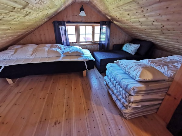 A cozy attic bedroom with two beds, a window, and a wooden ceiling.