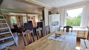 Une pièce chaleureuse avec un plancher en bois, une table à manger avec des chaises, une échelle et une fenêtre donnant sur un paysage verdoyant.