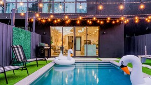 A modern house with a swimming pool, string lights, and inflatable swan decorations.