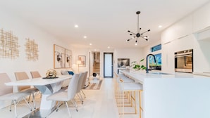 A modern kitchen with white cabinetry, a central island, and a dining area with a white table and chairs.
