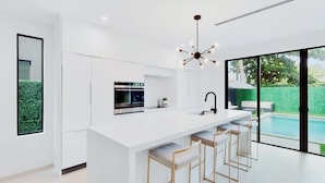 A modern kitchen with a central island, bar stools, and a large window overlooking a pool.