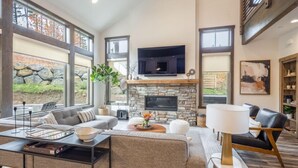 A spacious living room with a stone fireplace, large windows, and modern furniture. - Family Friendly w/ Suncadia Pool Access (Cle Elum)