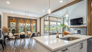 A modern kitchen with a large island, stone backsplash, and a dining area with natural light. - Family Friendly w/ Suncadia Pool Access (Cle Elum)