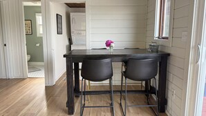 A kitchen with a wooden table and two chairs, a window with a view, and a door leading to a bathroom.