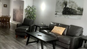 A modern living room with a dark leather sofa, a coffee table, and a dining area with a wooden table and chairs.