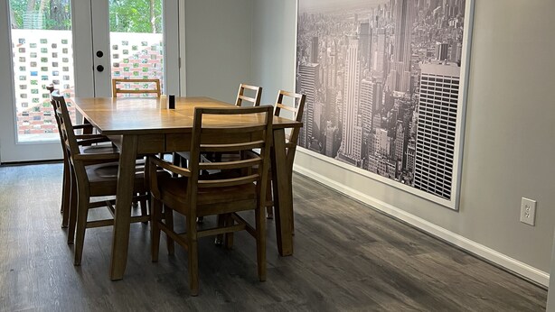 A dining area with a wooden table and chairs, a cityscape mural on the wall, and a view of the outdoors through glass doors.