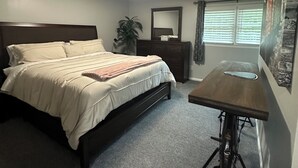 A bedroom with a bed, bedside table, dresser, and a small desk with a chair.