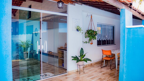Una habitación con puerta corredera de vidrio, suelo de madera, una mesa pequeña con una silla y una planta colgante.