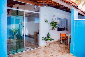 A room with a glass sliding door, a wooden floor, a small table with a chair, and a hanging plant. - Ribeiro Lugar de Paz Casa 2 (Arraial do Cabo)