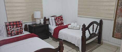 A hotel room with two beds, a nightstand, a lamp, and a wall with artwork.
