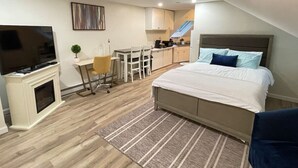 A bedroom with a bed, a TV, a desk, and a kitchenette.