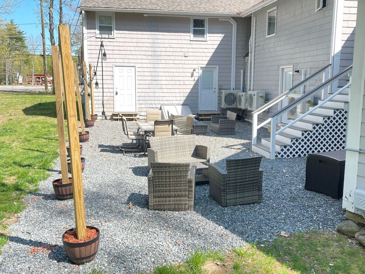 Un patio con mobiliario exterior, un columpio de madera y una casa con escaleras y equipos de aire acondicionado.