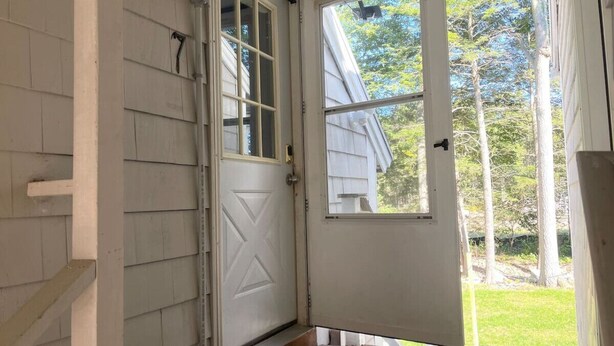A white door with a window, a welcome mat, and a wooden porch.