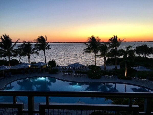 A poolside view at sunset with palm trees and lounge chairs.