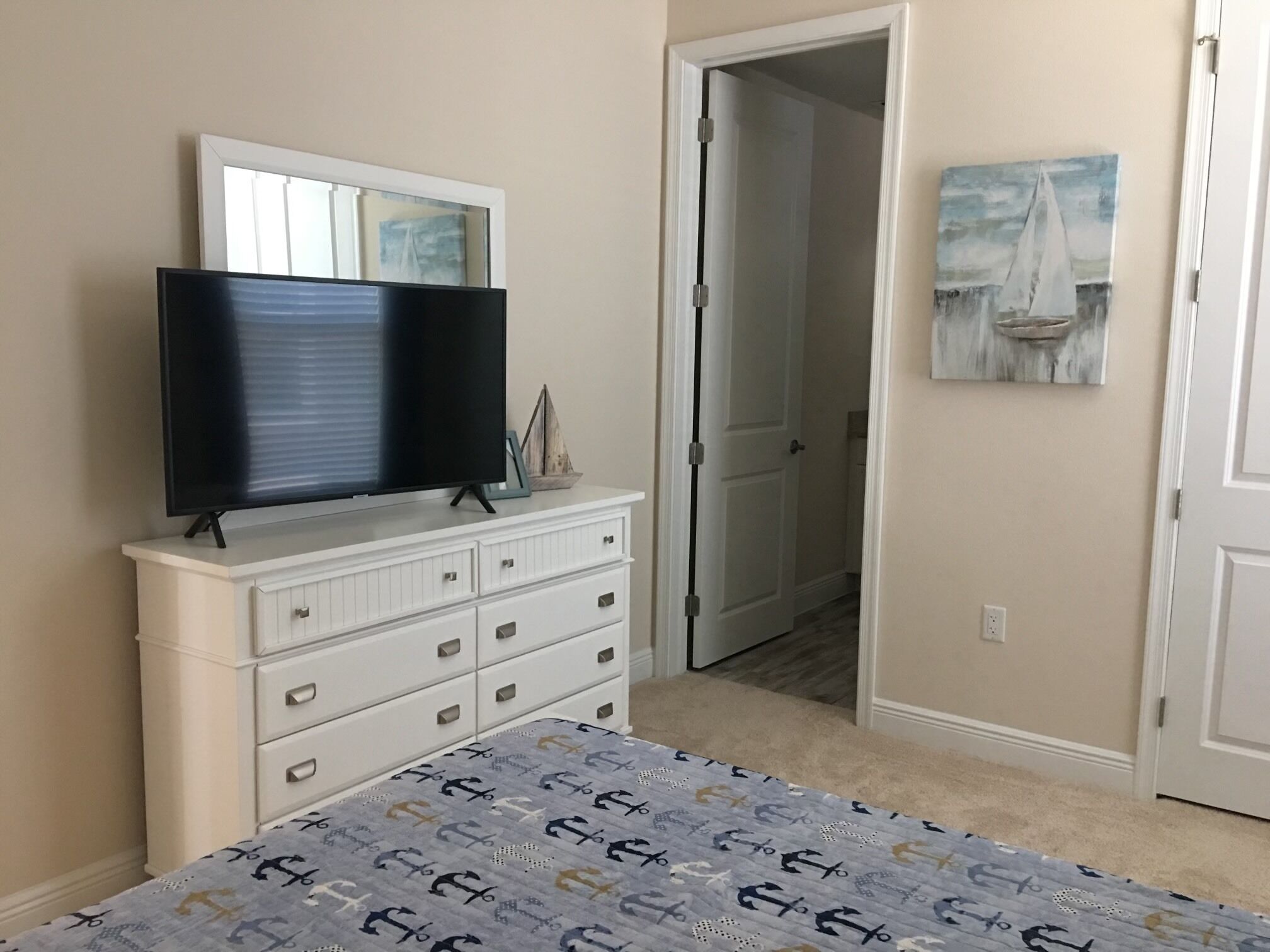 A bedroom with a bed, a dresser, a television, and a door leading to another room.