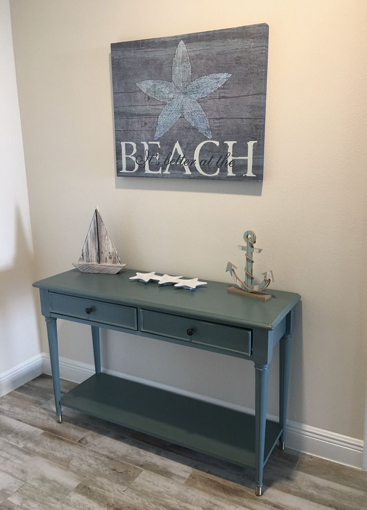 Un escriptori blau maragda amb calaixos, una decoració de estrella de mar i un petit model de vaixell a la paret de dalt.