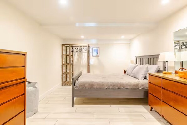 Ein Schlafzimmer mit Bett, Holzkommode und Spiegel.