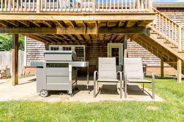 Ein überdachter Außenbereich mit Holzdeck, Grill, zwei Stühlen und einem kleinen Tisch.