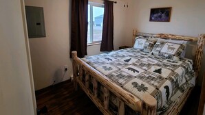 Ein Schlafzimmer mit einem Bettgestell aus Holz, einem Deckenventilator, einem Fenster mit Vorhängen und einer Wandleuchte.
