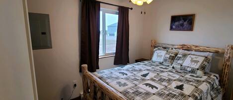 Un dormitorio con estructura de cama de madera, ventilador de techo, ventana con cortinas y lámpara fijada a la pared.