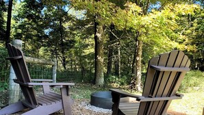 Two Adirondack chairs in a forested area with a wooden deck and a wire fence. - Wildflower Paradise: Luxury Lodge Suite in Amish Country (Dundee)