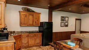 A kitchen with wooden cabinets, a black refrigerator, and a dining area with a table and chairs. - Adventure Awaits Suite: Luxury, Lodge Suite in Amish Country, Ohio. (Dundee)