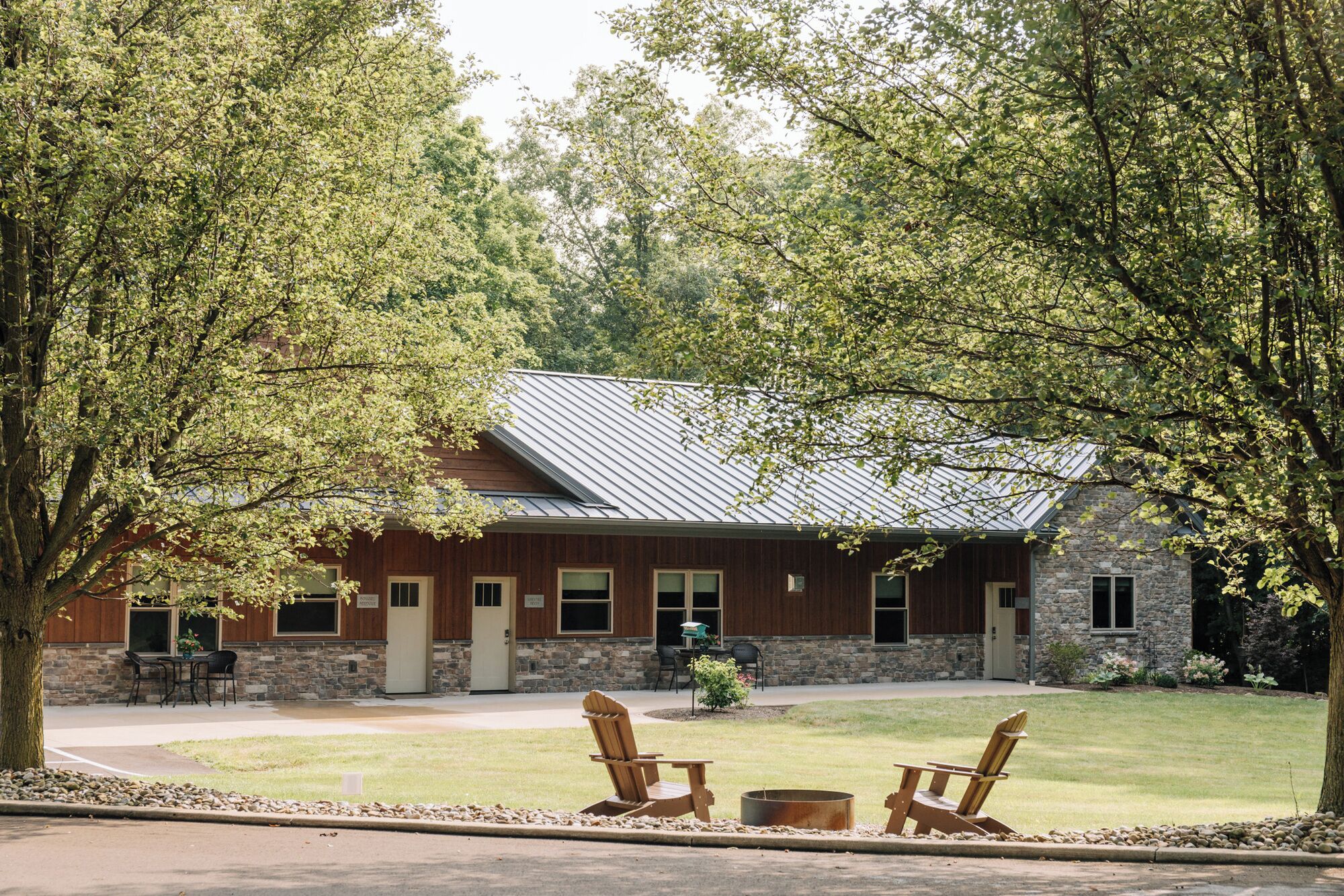 A lodge with a stone facade, a metal roof, and a patio area with Adirondack chairs.