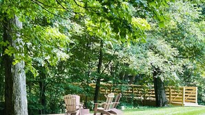 Un patio trasero con una terraza de madera, dos sillas Adirondack y una pequeña mesa.