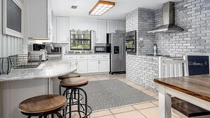 Una cocina moderna con armarios blancos, una pared decorativa de ladrillo, una estufa empotrada y una zona de bar con taburetes.