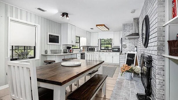 Una cocina moderna con armarios blancos, una mesa de comedor de madera y una chimenea de piedra.