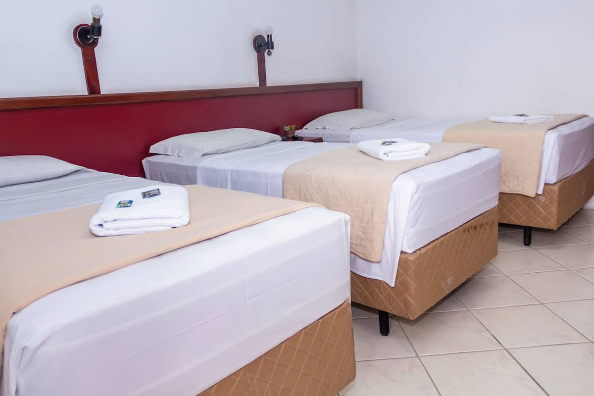 A hotel room with four single beds, each with a white mattress and a beige blanket.