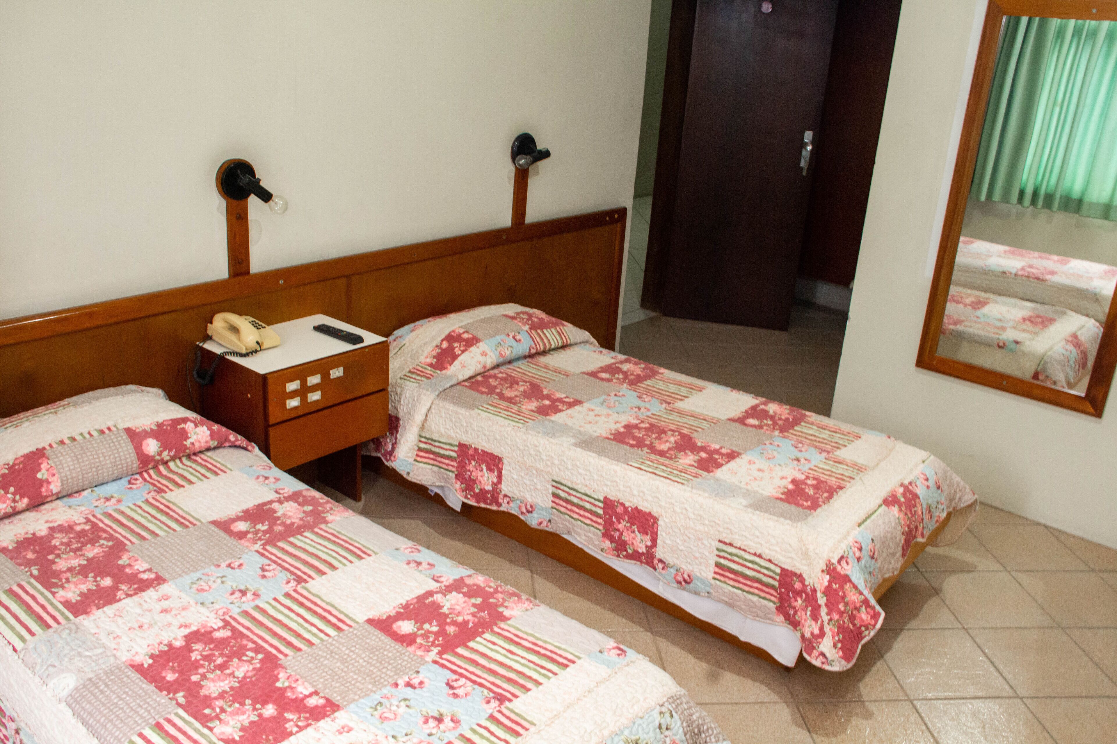 Un dormitorio con dos camas individuales, una mesita de noche con lámpara, teléfono y espejo.