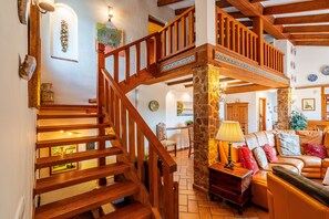 Eine Holztreppe mit einer Stein Säule, ein Sofa mit Kissen und ein Essbereich mit Tisch und Stühlen.