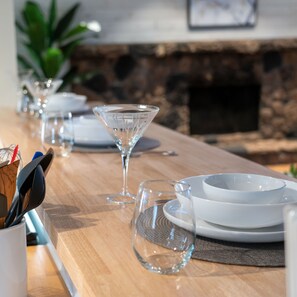A dining table set with clear glassware, plates, and a bowl, with a stone wall and greenery in the background.