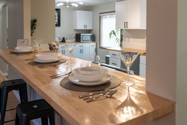 A kitchen with a wooden countertop, white cabinets, and a dining area set with plates, glasses, and cutlery.