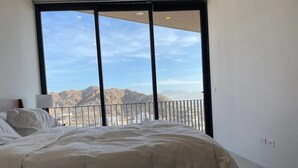 A bedroom with a large bed, a nightstand, and a view of mountains through a balcony. - CONDO P1 BY TRVL2HM (Cabo San Lucas)