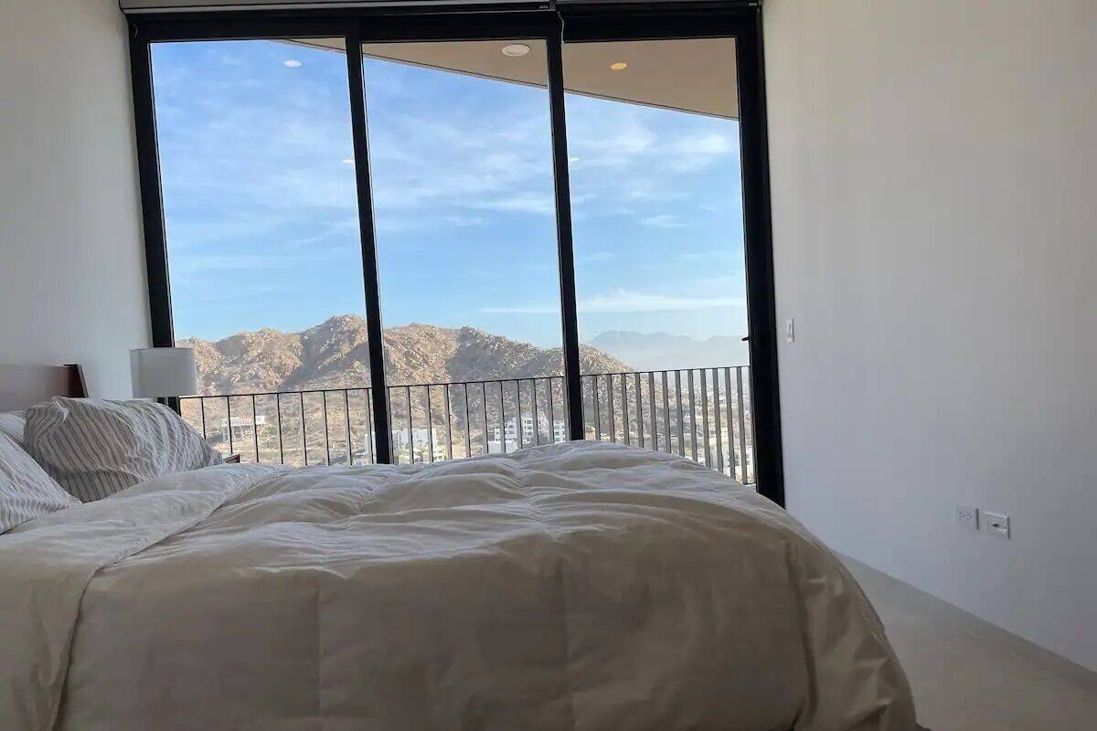 A bedroom with a large bed, a nightstand, and a view of mountains through a balcony.