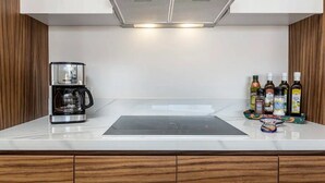 A kitchen with a coffee maker, a range hood, and a countertop with bottles and a tray of condiments. - CONDO P1 BY TRVL2HM (Cabo San Lucas)