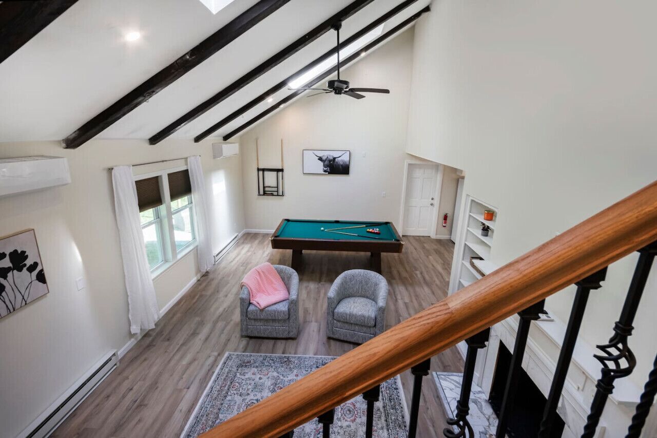 A spacious room with a pool table, two armchairs, a ceiling fan, and a view of the outdoors.