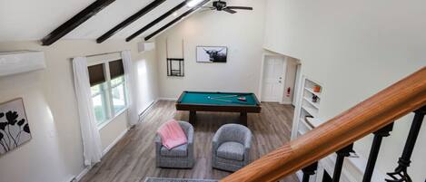 A spacious room with a pool table, two armchairs, a ceiling fan, and a view of the outdoors.